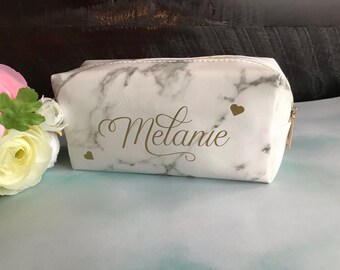 May include: White marble makeup bag with a gold zipper and the name "Melanie" printed in gold lettering. Two small gold hearts are on either side of the name.