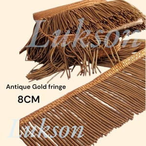 May include: Antique gold fringe, 8 cm long, with a textured, woven design. The fringe is a warm, metallic gold colour, perfect for adding a vintage touch to crafts and sewing projects. The text "Antique Gold fringe" and "8CM" are visible.