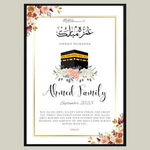 Pode incluir: Um cartão branco com uma borda dourada e detalhes florais. O cartão apresenta uma ilustração em preto e dourado da Caaba, um local sagrado em Meca, Arábia Saudita. O texto "Umrah Mubarak" está escrito em árabe no topo do cartão, e o texto "Ahmed Family" está escrito em uma fonte decorativa abaixo da ilustração. A data "Setembro de 2023" está escrita abaixo do nome da família. O cartão também inclui uma oração em inglês que diz: "May Allah (SWT) accept your Umrah, and grant you mercy and forgiveness from it. May Allah (SWT) reward you for your efforts and may the blessing and serenity of the holy lands always remain with you. Ameen."