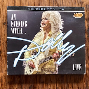 May include: A DVD and CD set titled "An Evening With... Dolly" featuring a live performance. The cover shows Dolly Parton in a gold outfit playing a guitar, with the word "Dolly" in a stylized font.