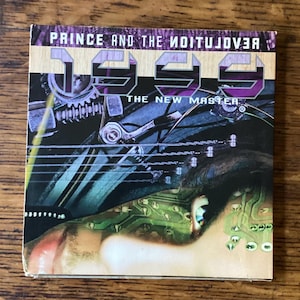 May include: A CD case with the album title "1999" by Prince and The Revolution. The cover art features a futuristic design with a face and circuit board elements, in shades of purple, green, and silver.