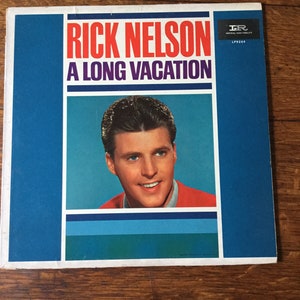 May include: A vintage vinyl record album cover featuring Rick Nelson. The cover is blue and white with a red stripe. The album title is "A Long Vacation" and the record label is Imperial High Fidelity. The cover features a photo of Rick Nelson in a red sweater.
