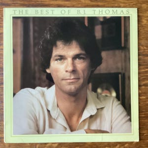 May include: Album cover for "The Best of B.J. Thomas." The cover features a portrait of a man with dark hair and a light-colored shirt. The title is printed in green at the top of the cover.