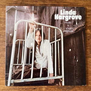 May include: A white ceramic mug with a black handle and the text "But First, Coffee" in a black, bold font. The mug is on a white surface. The mug is approximately 10 cm tall.