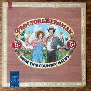 May include: A vintage record album cover featuring two men in a field. The album cover is brown with a red oval in the center. The oval contains the text "Proctor & Bergman" and "What This Country Needs". The men are wearing casual clothing and are holding money and a cigar. The album cover also features the text "A Good 5¢ Joke" in two places.