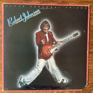 May include: A vinyl record album cover featuring Robert Johnson, a musician playing a red electric guitar. The album title is "Close Personal Friend".