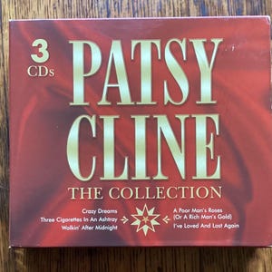 May include: A square 3-CD collection box set by Patsy Cline with a deep red background. The text reads PATSY CLINE THE COLLECTION, 3 CDs, and lists song titles including Crazy Dreams, Three Cigarettes In An Ashtray, Walkin' After Midnight, A Poor Man's Roses (Or A Rich Man's Gold), and I've Loved And Lost Again.