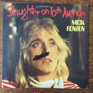 May include: Album cover for "Slaughter on 10th Avenue" by Mick Ronson. The cover features a portrait of a person with long blonde hair, wearing a red and white striped shirt. The album title is in red, and the artist's name is in yellow.