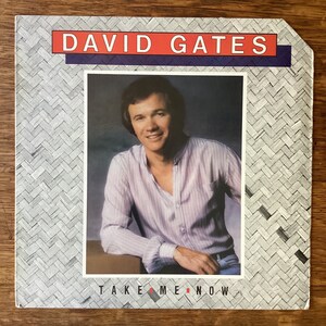 May include: Album cover featuring David Gates, with the text "DAVID GATES" in red and white. The album cover has a photo of David Gates wearing a light purple striped shirt. The text "TAKE ME NOW" is at the bottom.