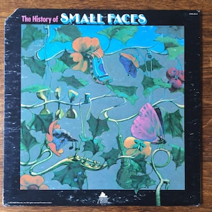 May include: The History of Small Faces album cover featuring a psychedelic illustration of a blue sky with green vines, flowers, butterflies, and musical instruments. The album title is printed in white letters on a black background.