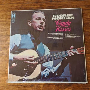 May include: A vinyl record album cover featuring George Morgan. The cover art shows a man playing a guitar. The album title is "Candy Kisses". The album cover is in a blue and white color scheme.