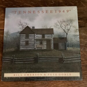 May include: A vintage record album cover featuring a painting of a white and brown log cabin with a wooden fence in front. The album title is "Tennessee 1949" and the artists are Bill Emerson & Pete Goble.