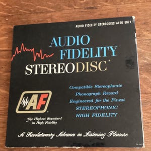 May include: A black Audio Fidelity Stereodisc record cover with white and blue text. The cover features the words "AUDIO FIDELITY STEREODISC" and the logo "AF". The text also includes "Compatible Stereophonic Phonograph Record".