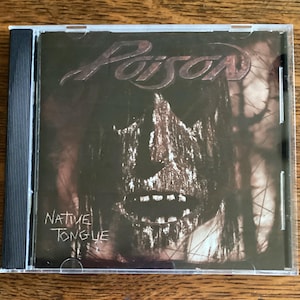 May include: A CD case with a black background and a close-up of a wooden face with a dark, textured surface. The text "Poison" is in white lettering at the top of the case and "Native Tongue" is in white lettering at the bottom of the case.