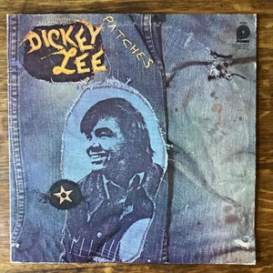 May include: Vintage vinyl record album cover for Dickey Lee's "Patches." The cover has a denim-style background with patches. The artist's name is in a yellow and orange patch, and a portrait of the artist is in a blue patch.