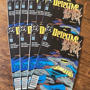 May include: A collection of DC Comics' Detective Comics, issue #605, featuring Batman. The comic book covers are black with the title in yellow and the image of Batman in a blue and gray color scheme. The comics are stacked on a wooden surface.