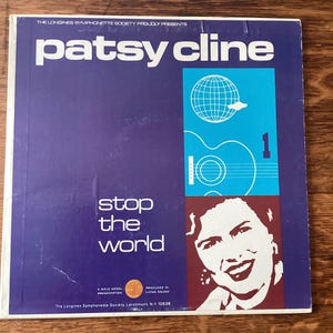 May include: A vintage Patsy Cline album cover with a purple background. The album title "Patsy Cline" is in white, above the words "stop the world". The cover features a guitar, globe, and a portrait of Patsy Cline.