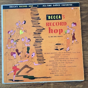 May include: Vintage vinyl record album cover titled "Decca's Record Hop" with cartoon illustrations of dancing couples. The cover is orange with black and yellow text, and features a stack of records.