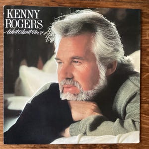 May include: A vintage vinyl record album cover featuring Kenny Rogers with the title "What About Me?" in white text. The album cover features a close-up portrait of Kenny Rogers with a white background.