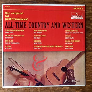 Peut inclure: Pochette de l'album vinyle vintage "All-Time Country and Western" de divers artistes. La couverture présente une bannière rouge avec les titres des chansons et les noms des artistes, ainsi qu'une illustration de violon, de guitare et de botte de cowboy.