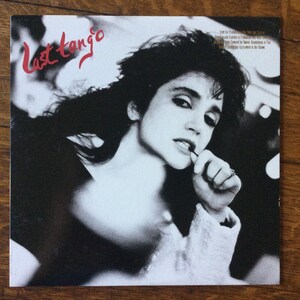 May include: Black and white photo of a woman with dark hair, wearing a white shirt, looking at the camera and biting her fingernail. The text "Last Tango" is written in red at the top of the image.