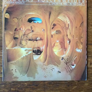 May include: A record album cover featuring a cave-like interior with a sandy floor and rock formations. The album title "Caverna Magica" and the artist's name "Andreas Vollenweider" are printed on the cover.
