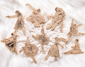 May include: Nine brown paper stickers featuring illustrations of dancers in various poses. The stickers are arranged on a white fuzzy surface.