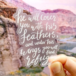 Puede incluir: Una pegatina transparente con letras blancas que dice "he will cover you with his feathers, and under his wings you will find refuge".