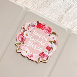 May include: Pink floral sticker with the text "Thankful Grateful Blessed" in white cursive lettering.