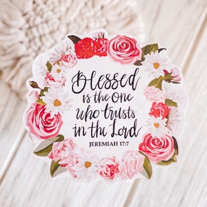 May include: A white sticker with a floral wreath border. The wreath is made of pink and white roses and daisies. The text in the center reads "Blessed is the one who trusts in the Lord, Jeremiah 17:7".