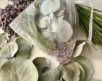 May include: A white sheer organza drawstring pouch filled with dried eucalyptus leaves, lavender buds, and pine needles. Additional loose dried eucalyptus leaves, lavender buds, and pine needles are scattered around the base of the pouch.