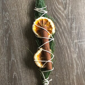 Peut inclure: Faisceau aromatique compos&eacute; d'une brindille de conif&egrave;re, d'un b&acirc;ton de cannelle et de deux tranches d'orange s&eacute;ch&eacute;es, le tout li&eacute; avec de la ficelle blanche. L'ensemble d&eacute;gage une esth&eacute;tique rustique et naturelle.