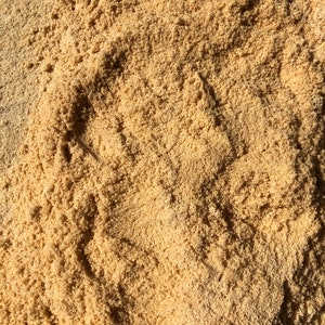 May include: A close-up shot of light brown sand, showing a textured, granular surface. The sand's colour varies slightly, with shadows adding depth. The image focuses on the texture and colour of the sand, suggesting a natural environment.