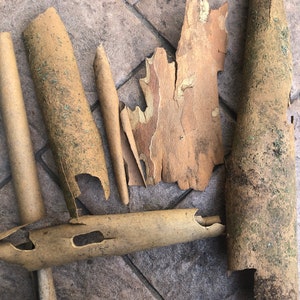 May include: Overhead view of assorted tree bark pieces in brown and tan hues. The bark is laid out on a textured, grey surface. Some pieces are long and cylindrical, others are flat and irregularly shaped, showing natural textures and patterns.