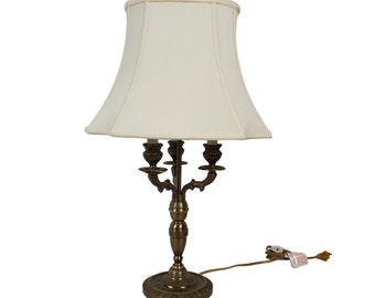May include: A brass table lamp with a white fabric lampshade. The lamp has a candelabra style base with four arms and a decorative finial.