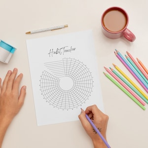 Puede incluir: Un rastreador de hábitos blanco con un círculo dividido en secciones para el seguimiento diario. Una persona está coloreando las secciones con un lápiz morado. También hay lápices de colores en varios colores pastel sobre la mesa.