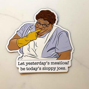 May include: A sticker featuring a cartoon illustration of a woman with brown hair and glasses, wearing a blue and white dress and yellow gloves. The text on the sticker reads: "Let yesterday's meatloaf be today's sloppy joes."