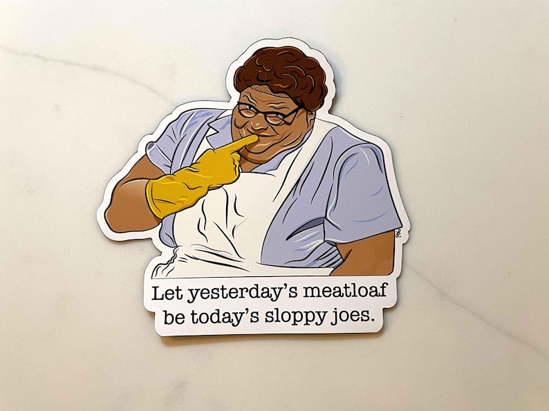 May include: A sticker featuring a cartoon illustration of a woman with brown hair and glasses, wearing a blue and white dress and yellow gloves. The text on the sticker reads: "Let yesterday's meatloaf be today's sloppy joes."