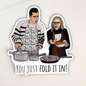 May include: A sticker featuring a cartoon illustration of two people in an apron, one stirring a pot and the other holding a bowl. The text "You just fold it in!" is below the image.