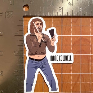May include: A cartoon illustration of a man with curly brown hair and a mustache playing a cowbell with a drumstick. He is wearing a brown shirt with a black belt, blue jeans, and a pair of glasses. The text "MORE COWBELL" is written below the image.