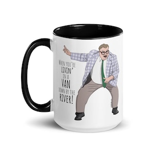 May include: White ceramic mug with a black interior and handle. The mug features a cartoon illustration of a man in a plaid jacket and the text "When you're livin' in a van down by the river!"