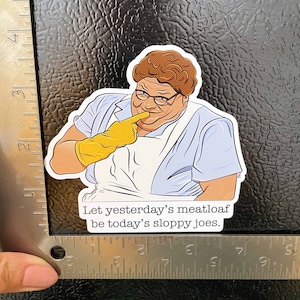 May include: A sticker featuring a cartoon illustration of a woman with brown hair and glasses wearing a blue shirt and yellow gloves. The text on the sticker reads "Let yesterday's meatloaf be today's sloppy joes."
