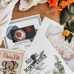 Pode incluir: Um close-up de uma página impressa com o título "Koalas Down Under". A página apresenta uma ilustração em aquarela de um coala sentado em um galho de eucalipto. O texto explica que os coalas são criaturas gentis e sonolentas que vivem nas florestas da Austrália. A página também inclui um mapa da Austrália.