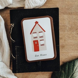 May include: A brown card with a white house illustration and red roof. The text "das Haus" is printed below the house.
