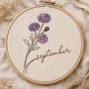 May include: An embroidered floral design in a wooden hoop. The design features purple flowers, green leaves, and the word "september" in brown thread. Ideal for home decor, this piece is a charming, handcrafted item.