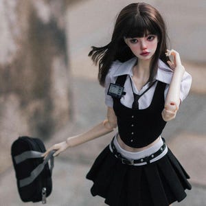 May include: A doll in a black and white school uniform, with a pleated skirt, vest, and collared shirt. The doll has dark hair and carries a black backpack. A small ID badge is attached to the shirt.