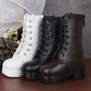 Könnte beinhalten: Zwei Paar Schnürstiefel, ein weißes und ein braunes Paar. Die Stiefel haben einen dicken Absatz und eine abgerundete Spitze.
