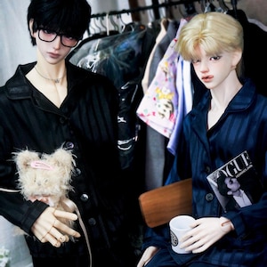 May include: Two dolls wearing pyjamas. One doll is wearing a black and white striped pyjama set and holding a small stuffed animal. The other doll is wearing a blue and white striped pyjama set and holding a magazine that says "Vogue" on the cover.