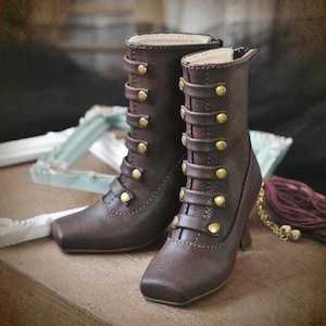 Può includere: Un paio di stivali in pelle marrone con dettagli e fibbie in metallo dorato. Gli stivali hanno un tacco alto e una punta quadrata. Il testo "SIZE: POP068 IP WONMEN HIGHHEEL" è visibile nell'immagine.