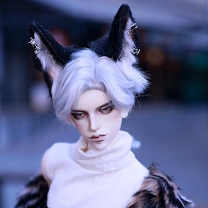 May include: A doll with white hair and black and white fur ears wearing a white turtleneck crop top and a brown and black fur jacket.